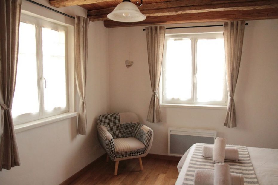 La chambre du rez-de chaussée avec des poutres anciennes en bois et un fauteuil dans une ambiance apaisante